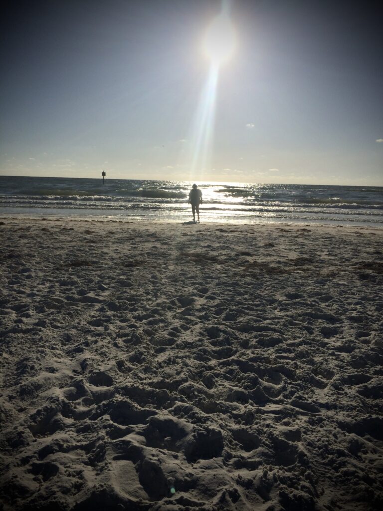 Beach and ocean. A ray of sunlight streams down on a woman in the distance