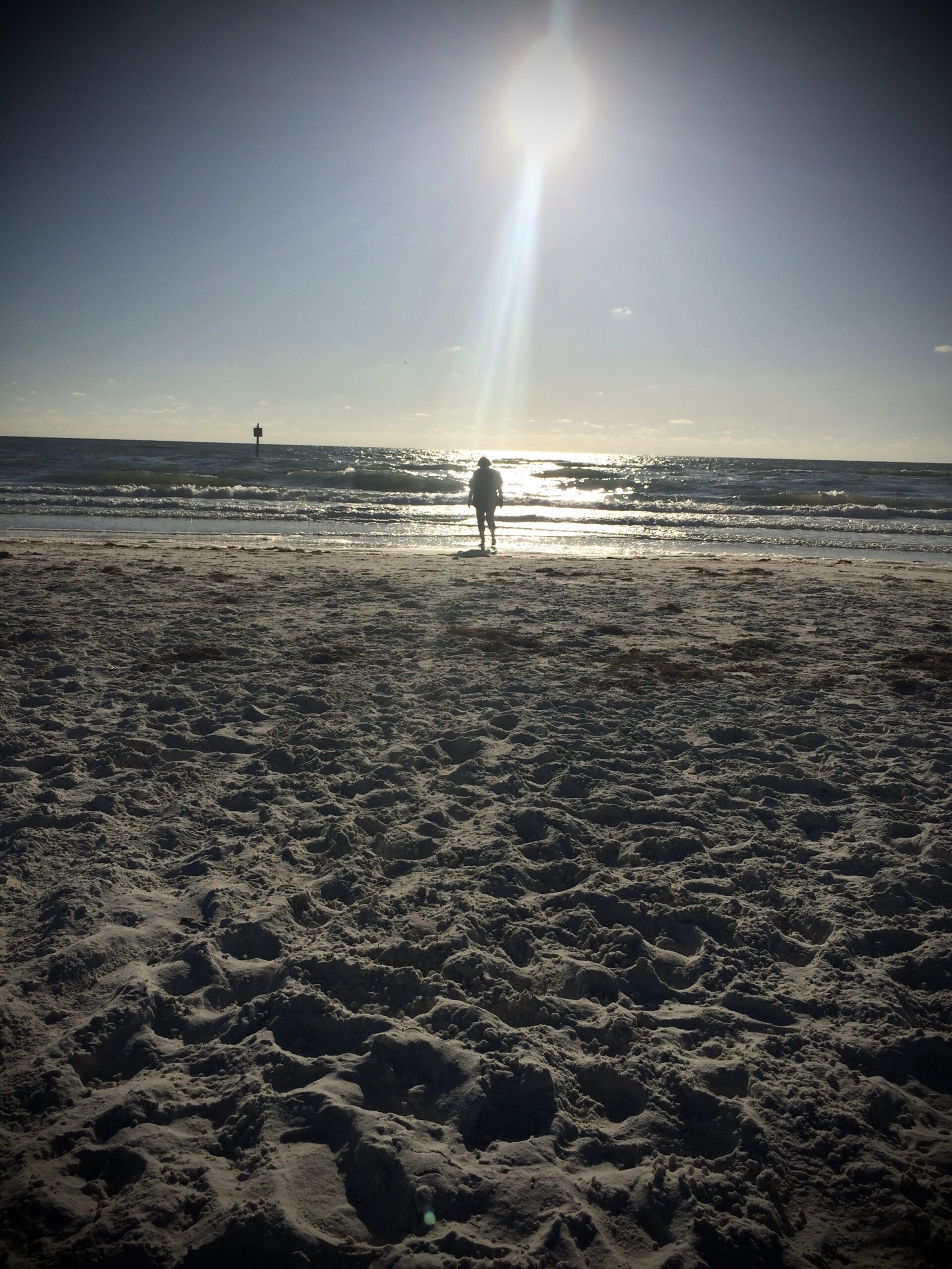 Beach and ocean. A ray of sunlight streams down on a woman in the distance